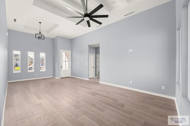 interior space with a tray ceiling, light hardwood / wood-style flooring, ceiling fan, and a towering ceiling