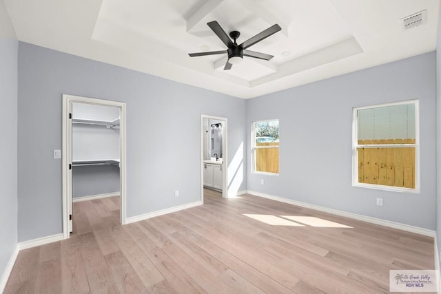 unfurnished bedroom featuring a raised ceiling, a spacious closet, sink, and light hardwood / wood-style flooring