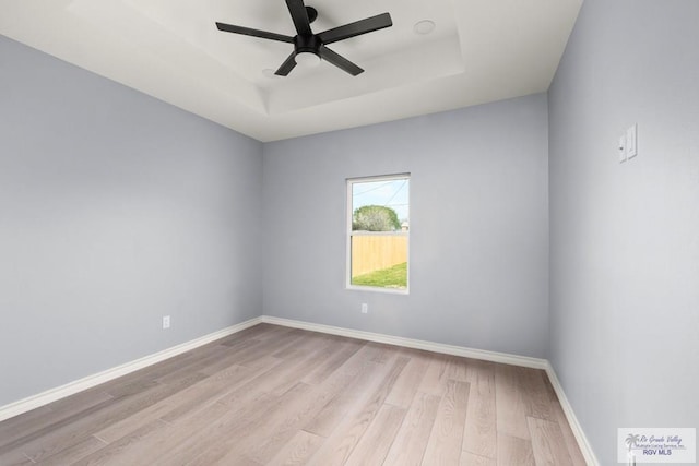 spare room featuring a raised ceiling, ceiling fan, and light hardwood / wood-style flooring