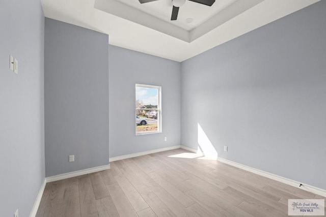 empty room featuring a raised ceiling, ceiling fan, and light hardwood / wood-style floors