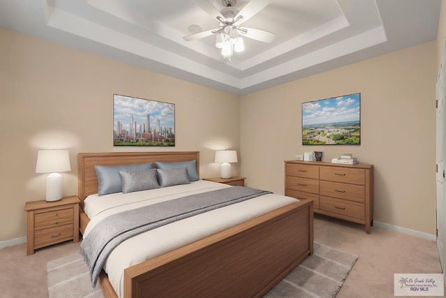 bedroom featuring light carpet, baseboards, a tray ceiling, and ceiling fan