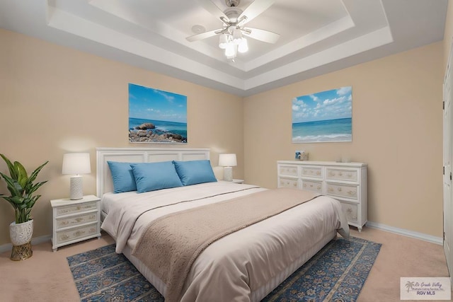 bedroom with a tray ceiling, light carpet, and baseboards