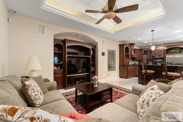 living room with a tray ceiling, light tile patterned floors, visible vents, ornamental molding, and ceiling fan