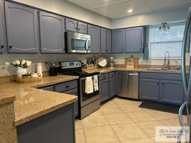 kitchen featuring appliances with stainless steel finishes, tasteful backsplash, sink, hanging light fixtures, and light tile patterned floors