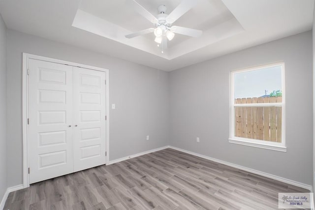 unfurnished bedroom with a closet, light hardwood / wood-style floors, a raised ceiling, and ceiling fan