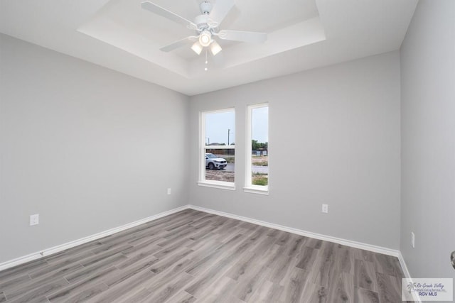 spare room featuring ceiling fan, light hardwood / wood-style floors, and a raised ceiling