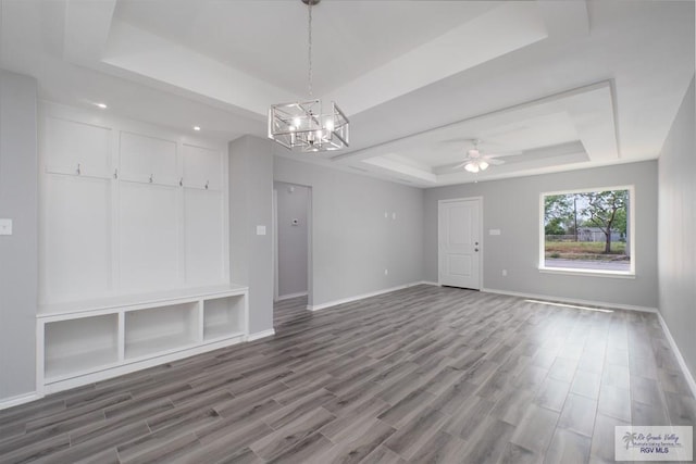 unfurnished living room featuring a tray ceiling, hardwood / wood-style floors, and ceiling fan with notable chandelier