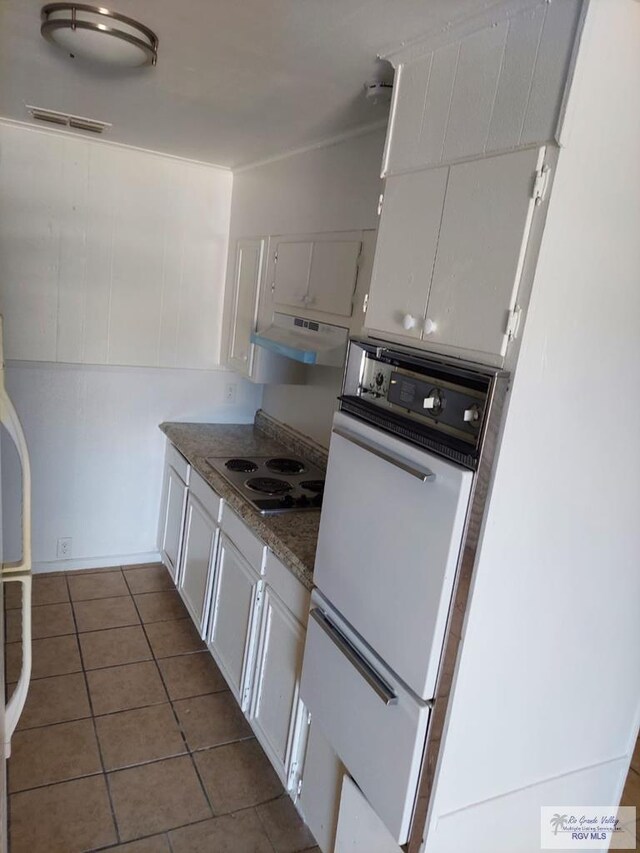 kitchen with white electric cooktop, dark tile patterned flooring, ventilation hood, and white cabinetry