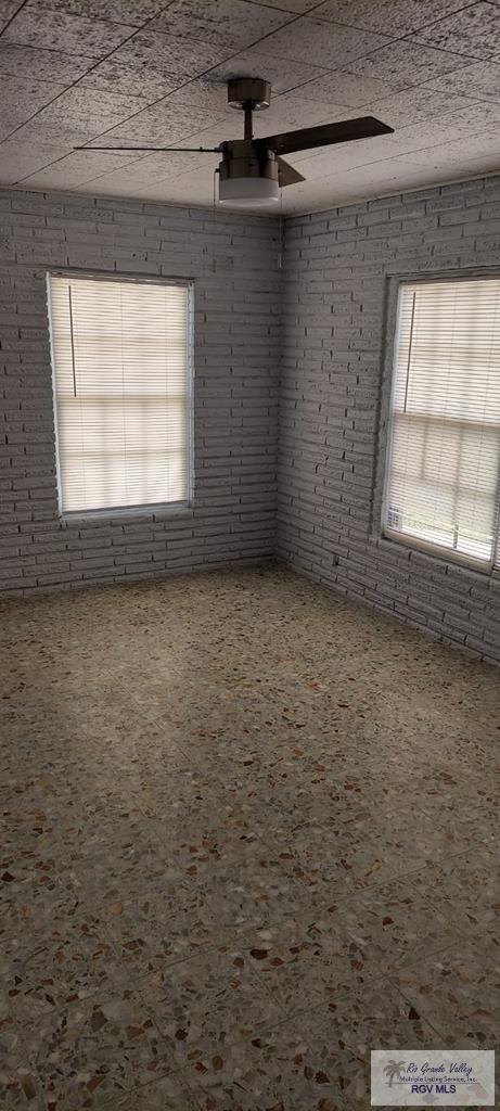 spare room with ceiling fan and brick wall