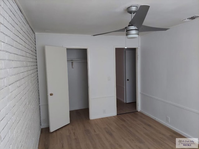 unfurnished bedroom featuring crown molding, hardwood / wood-style flooring, ceiling fan, brick wall, and a closet