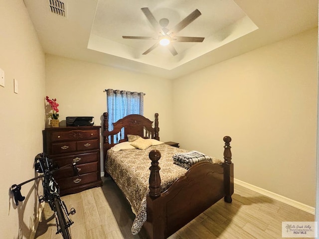 bedroom with light hardwood / wood-style flooring, a raised ceiling, and ceiling fan