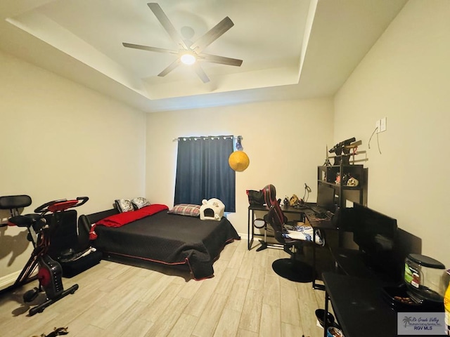 bedroom with a raised ceiling, ceiling fan, and light wood-type flooring