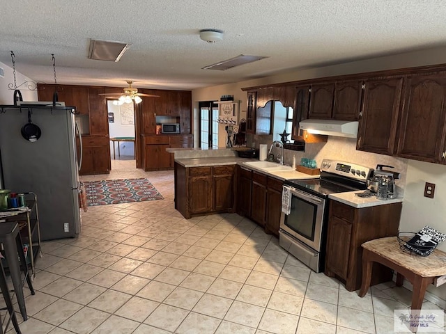 kitchen with a textured ceiling, a sink, light countertops, under cabinet range hood, and stainless steel appliances