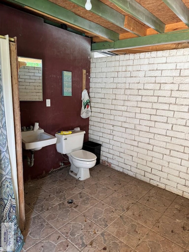 bathroom with a sink, toilet, and brick wall