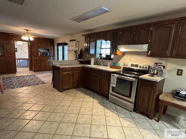 kitchen featuring a peninsula, light countertops, a textured ceiling, under cabinet range hood, and appliances with stainless steel finishes