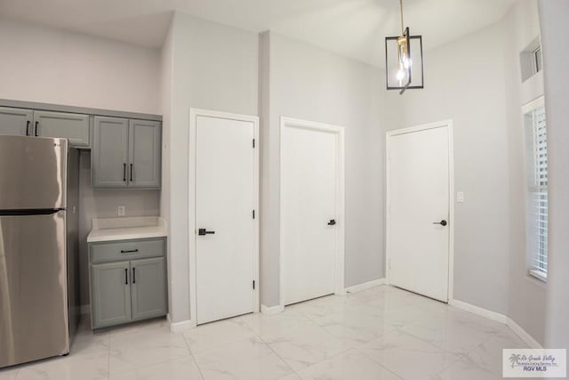 7549 Laurel Ave, Brownsville, TX 78526 - kitchen featuring freestanding refrigerator, gray cabinetry, light marble finish floors, light countertops, and pendant lighting
