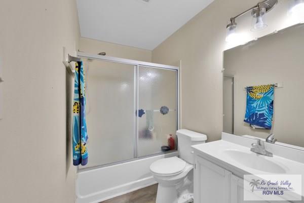 bathroom with toilet, enclosed tub / shower combo, wood finished floors, and vanity