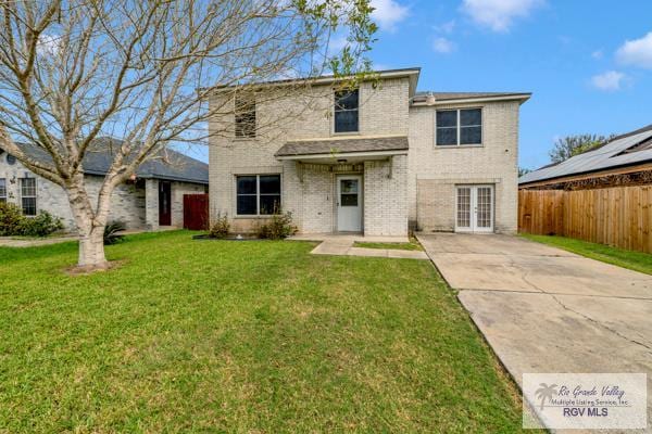 traditional home featuring french doors, a front yard, fence, and brick siding