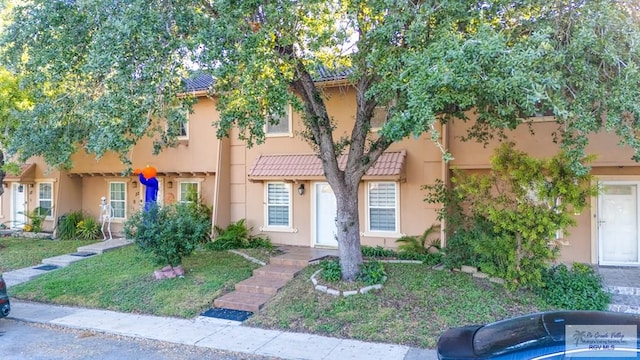 view of property featuring a front yard, a tile roof, and stucco siding