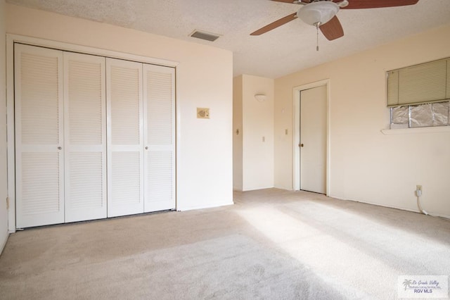 unfurnished bedroom featuring a closet, light colored carpet, visible vents, a ceiling fan, and a textured ceiling