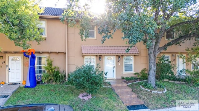 townhome / multi-family property with a tile roof, a front yard, and stucco siding