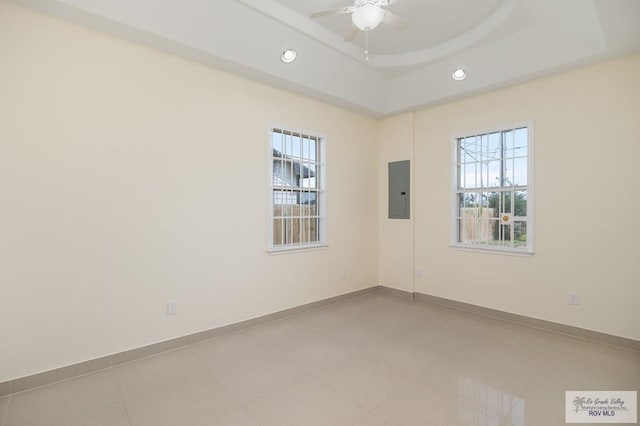 empty room with electric panel, a raised ceiling, and ceiling fan