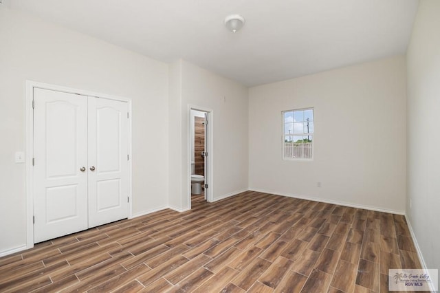 unfurnished bedroom featuring dark hardwood / wood-style floors, ensuite bath, and a closet