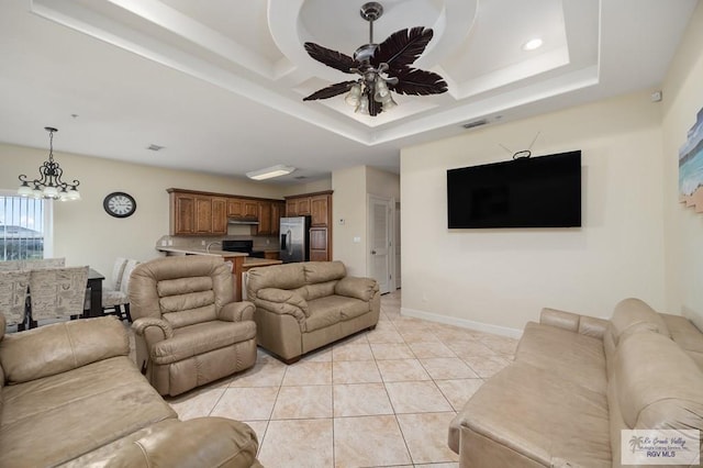 tiled living room with ceiling fan with notable chandelier and a tray ceiling