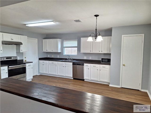 kitchen featuring dark hardwood / wood-style flooring, stainless steel appliances, an inviting chandelier, white cabinetry, and hanging light fixtures