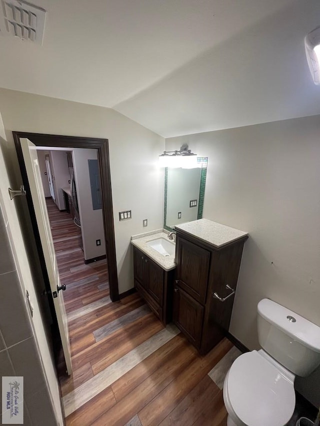 half bathroom featuring visible vents, lofted ceiling, toilet, wood finished floors, and vanity