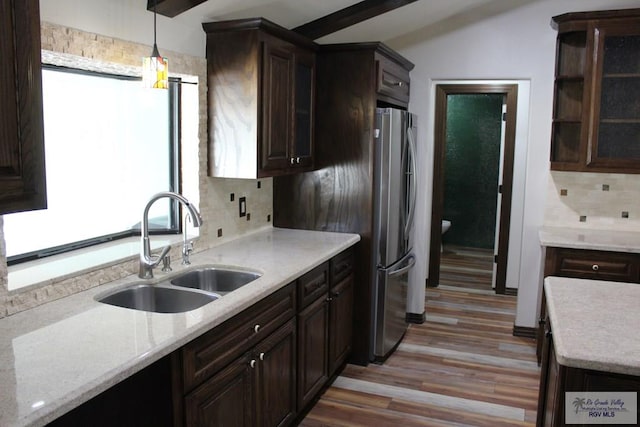 kitchen featuring tasteful backsplash, freestanding refrigerator, hanging light fixtures, dark brown cabinets, and a sink