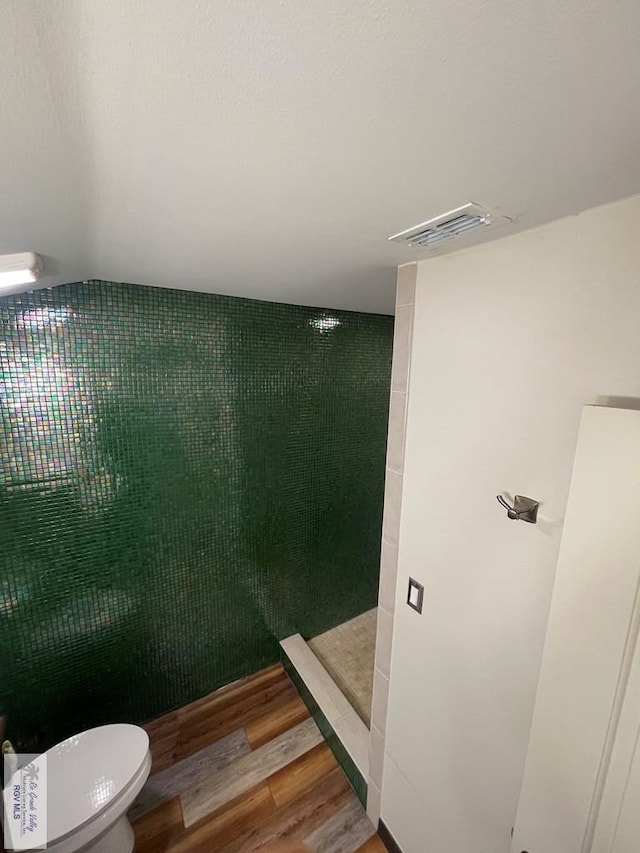 bathroom with toilet, visible vents, tiled shower, and wood finished floors