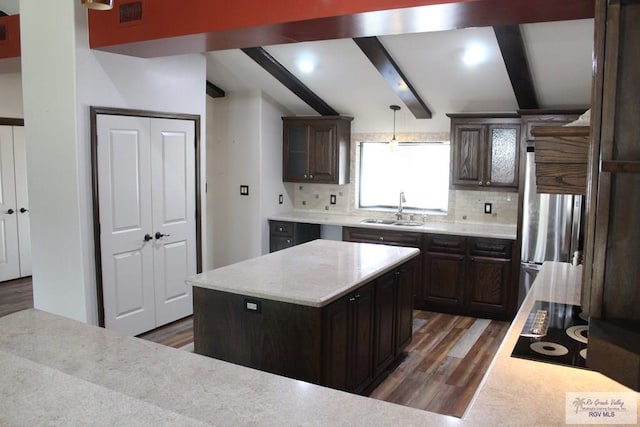 kitchen with visible vents, wood finished floors, vaulted ceiling with beams, a sink, and backsplash