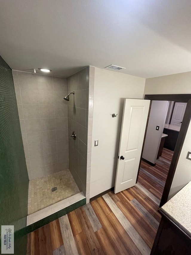 bathroom with wood finished floors, visible vents, vanity, baseboards, and tiled shower