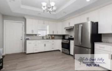 kitchen with a raised ceiling, light hardwood / wood-style floors, white cabinetry, stainless steel appliances, and a chandelier