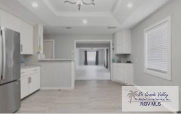 kitchen featuring white cabinetry, light hardwood / wood-style flooring, a notable chandelier, stainless steel fridge, and a tray ceiling