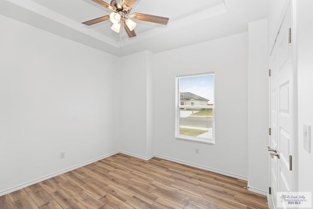 unfurnished room featuring ceiling fan, light hardwood / wood-style flooring, and a tray ceiling