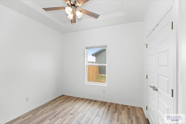 empty room featuring ceiling fan, a tray ceiling, and light hardwood / wood-style flooring