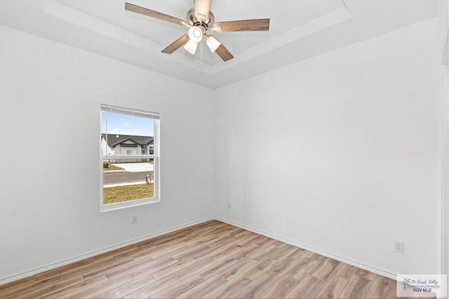 spare room with a tray ceiling, ceiling fan, and light hardwood / wood-style floors