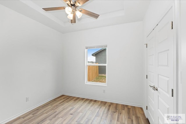 unfurnished room with a tray ceiling, ceiling fan, and light hardwood / wood-style flooring