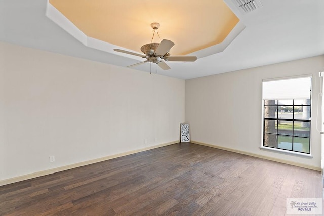 spare room with a raised ceiling, ceiling fan, and dark hardwood / wood-style flooring