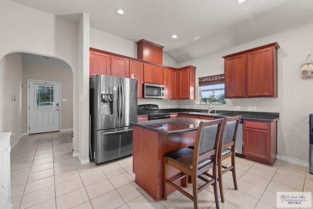 kitchen featuring arched walkways, stainless steel appliances, dark countertops, and a center island