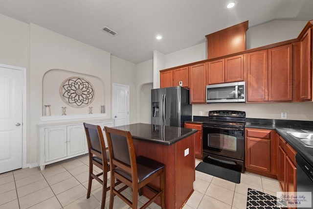 kitchen with light tile patterned floors, a kitchen island, visible vents, black appliances, and a kitchen bar