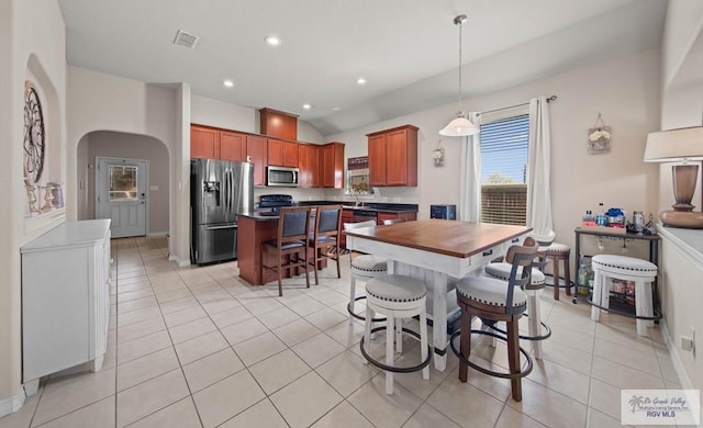 kitchen featuring light tile patterned flooring, stainless steel appliances, a kitchen breakfast bar, a center island, and dark countertops