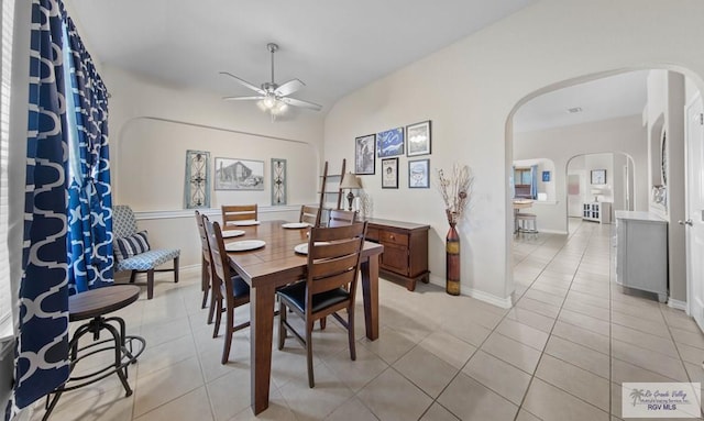 dining area with arched walkways, a ceiling fan, light tile patterned flooring, vaulted ceiling, and baseboards