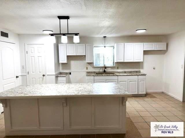 kitchen featuring light tile patterned flooring, decorative light fixtures, white cabinetry, sink, and a large island