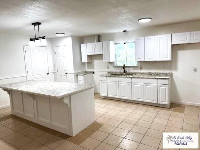 kitchen with hanging light fixtures, white cabinetry, a kitchen island, and sink