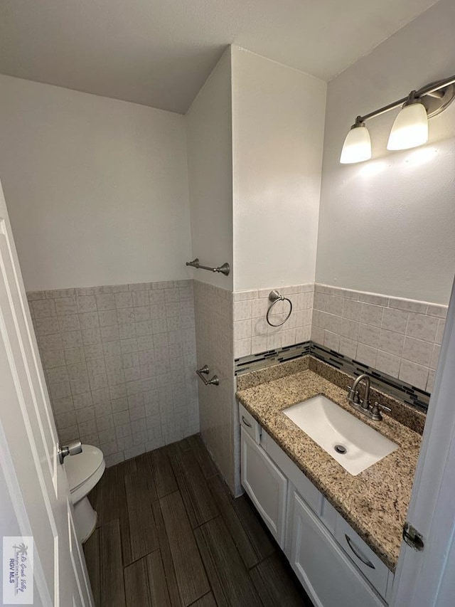 bathroom with wood-type flooring, vanity, toilet, and tile walls