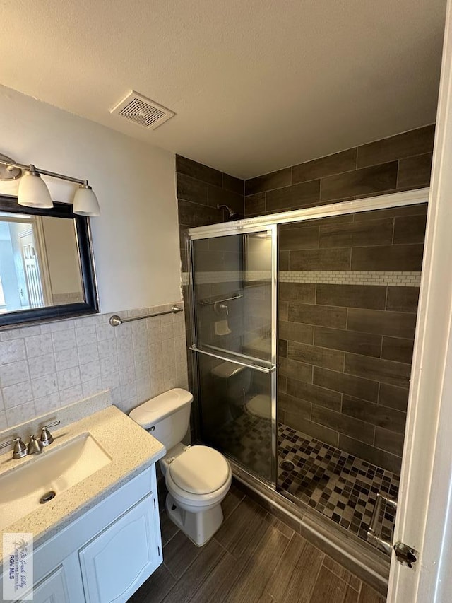 bathroom with toilet, a shower with door, vanity, tile walls, and hardwood / wood-style flooring