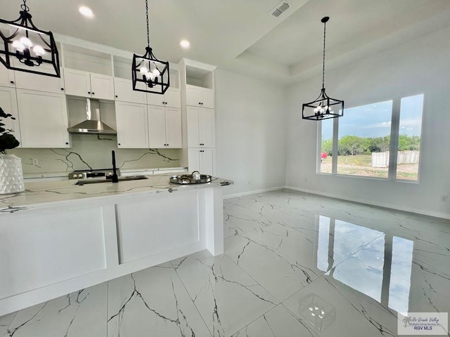 kitchen with white cabinets, sink, range hood, decorative light fixtures, and light stone counters